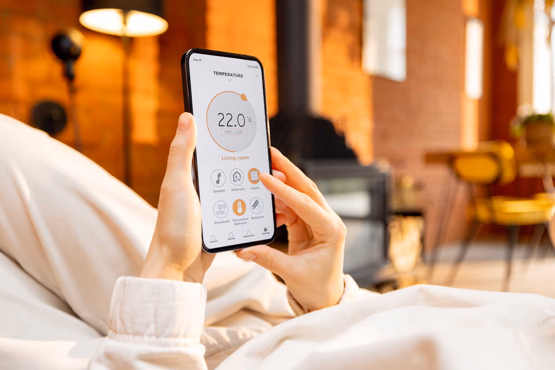 Person adjusts home temperature using a smartphone while sitting on a bed.