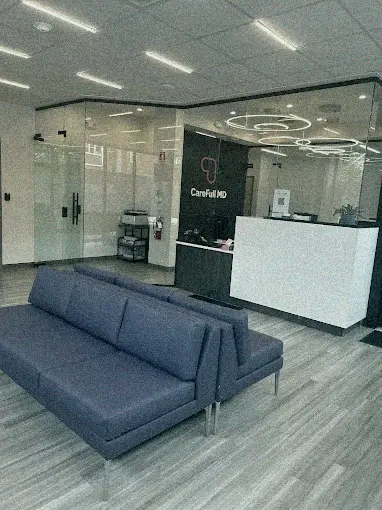 Modern clinic reception area with a white desk, circular ceiling lights, glass doors, and two navy blue sofas facing opposite directions.