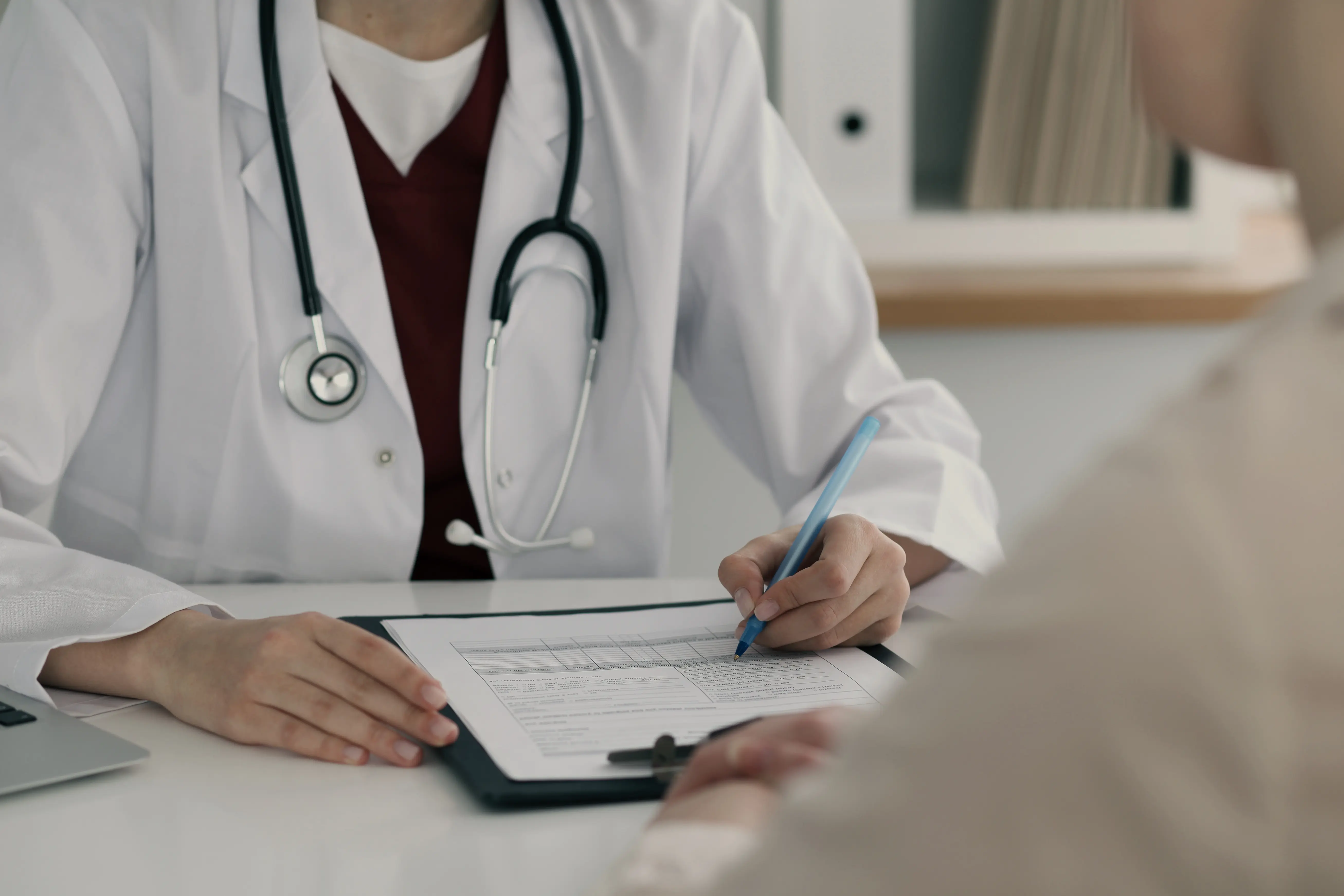 Male doctor with glasses and stethoscope smiling and showing a tablet to a young boy sitting on a couch.