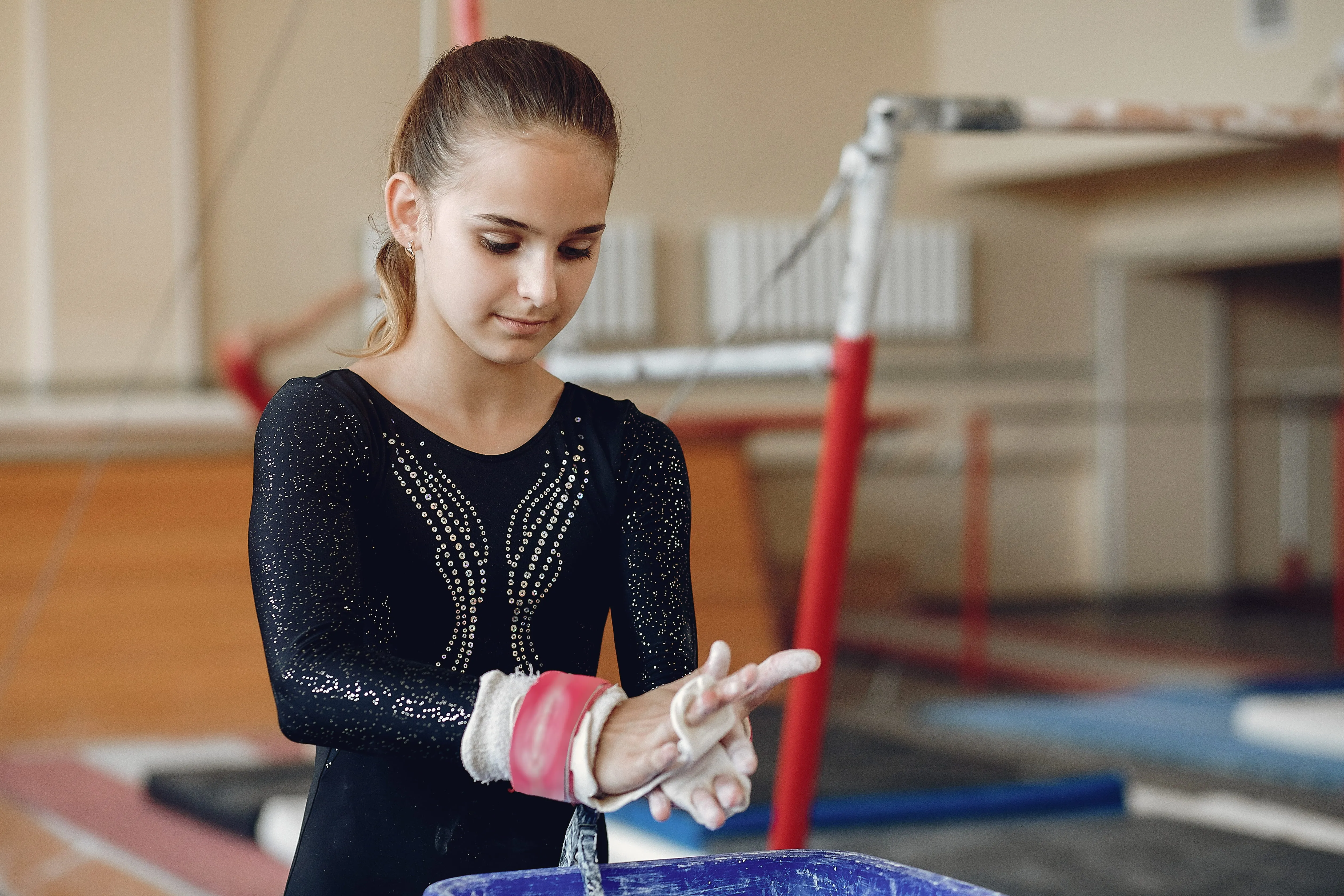 Young gymnast in a black leotard applying chalk to her hands in a gym.