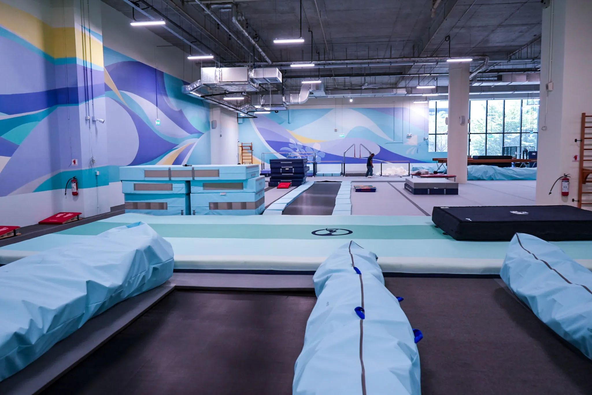 Indoor gymnastics training facility with trampolines, padded mats, and vibrant wall mural.