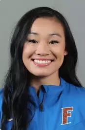 Portrait of a smiling woman with long black hair wearing a blue jacket with an 'F' emblem.