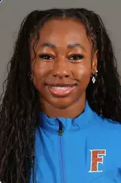 Smiling woman with long braided hair wearing a blue jacket with an embroidered letter F.