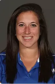 Smiling woman with long dark hair wearing a blue collared shirt against a dark background.