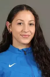 Portrait of a woman with long dark curly hair wearing a blue Nike jacket against a neutral background.