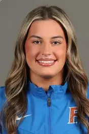 Portrait of a woman with long blonde and brown hair wearing a blue jacket with a logo on the left side.