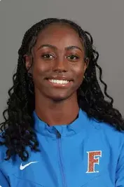 Smiling woman with curly hair wearing a blue Nike jacket with an orange and blue F logo.