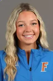Smiling young woman with long wavy blonde hair wearing a blue jacket with an orange and white 'F' logo.