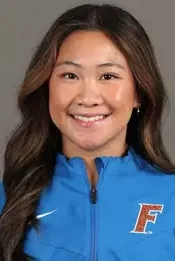 Smiling young woman with long brown hair wearing a blue zip-up jacket with an F logo.