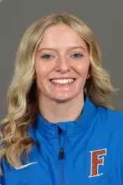 Smiling woman with blonde wavy hair wearing a blue jacket with an orange and blue 'F' logo.