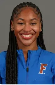 Smiling young woman with long braided hair wearing a blue jacket with an orange letter F emblem.
