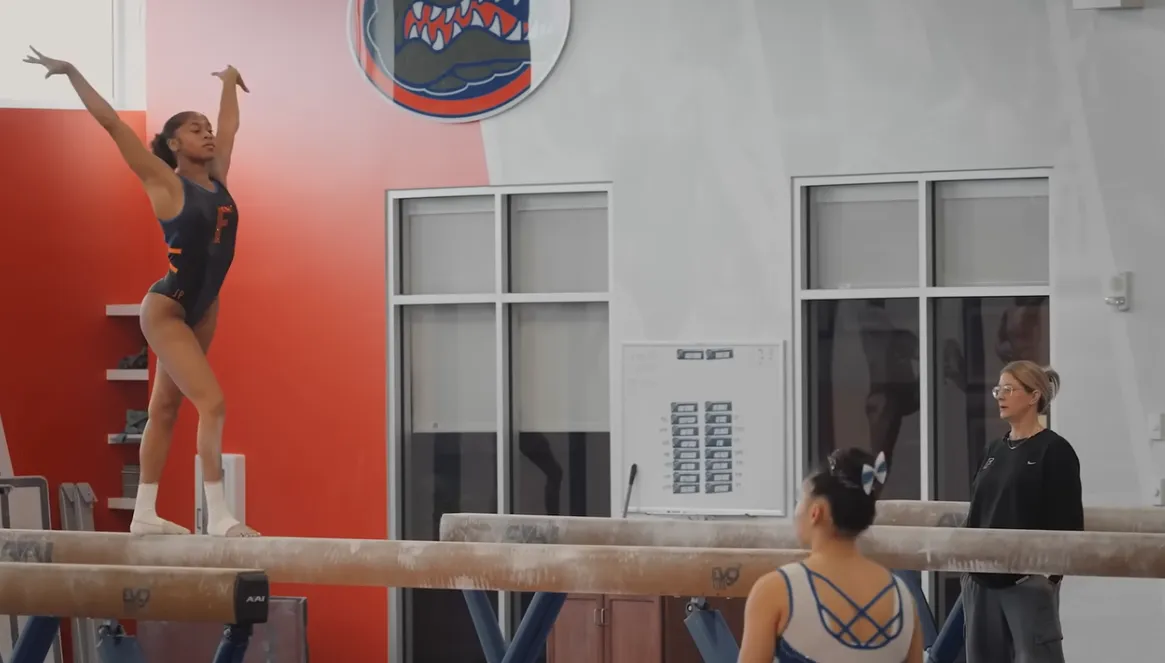 Gymnast performing an advanced handstand on parallel bars in an indoor gymnasium.