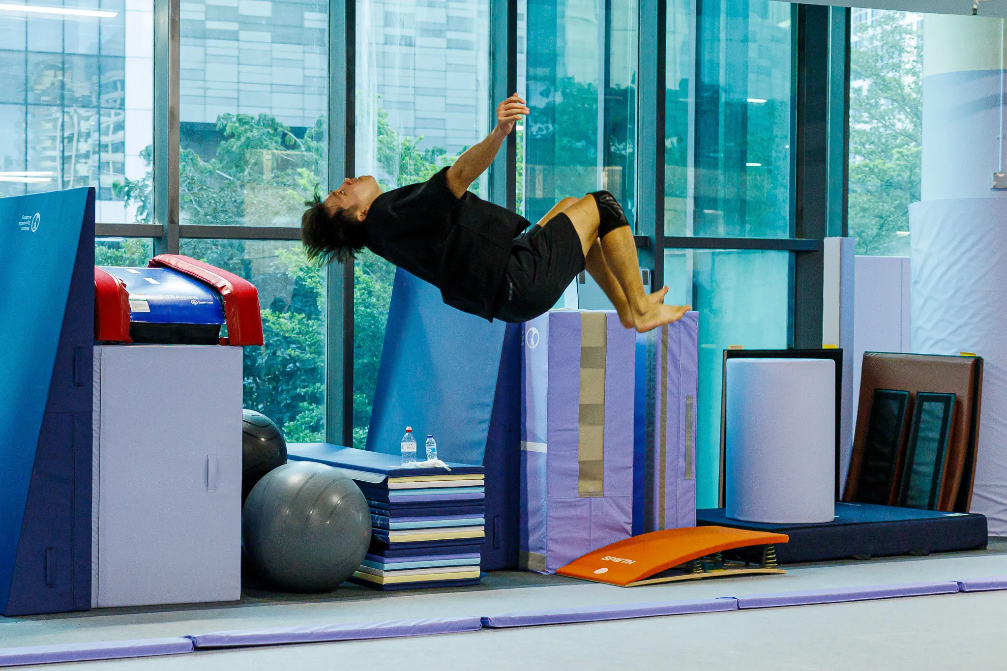 Shirtless man with tattoos performing a handstand on parallel bars in a gymnastics gym.