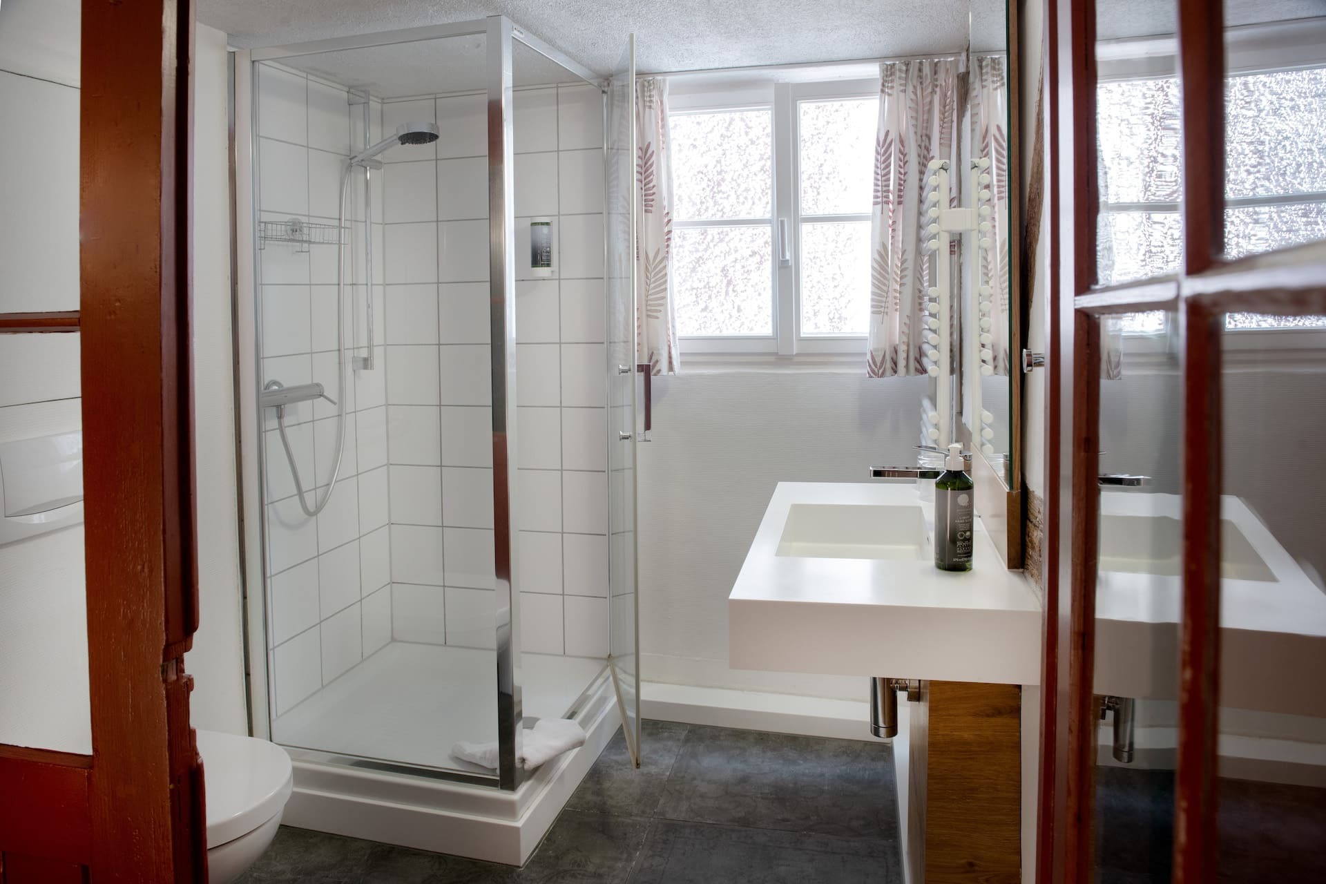 Badezimmer mit Toilette, Waschbecken, Spiegel und Dusche, Fenster