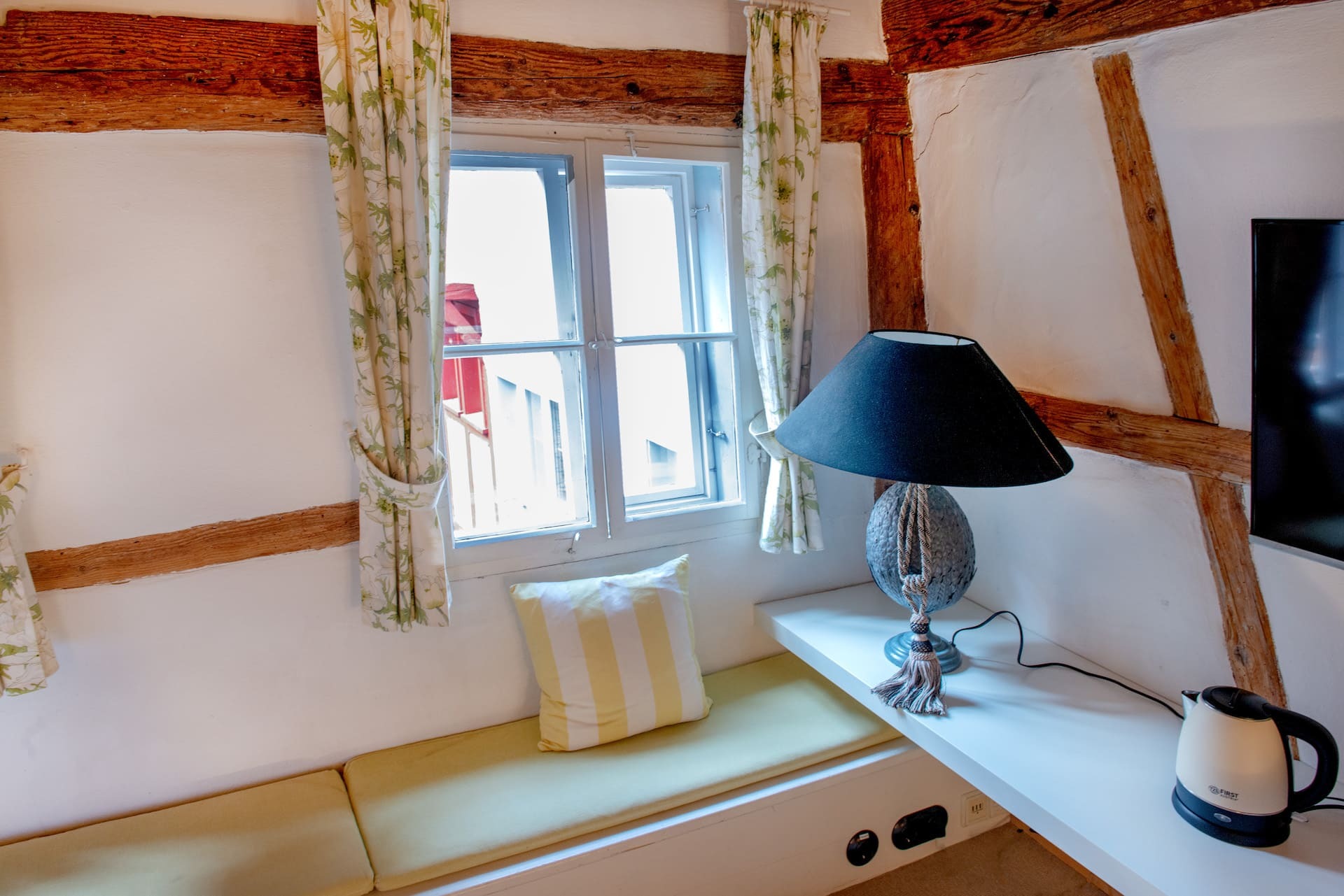 Sitzbank mit Dekokissen, Fenster mit Vorhang, Lampe, Wasserkocher, Fernseher