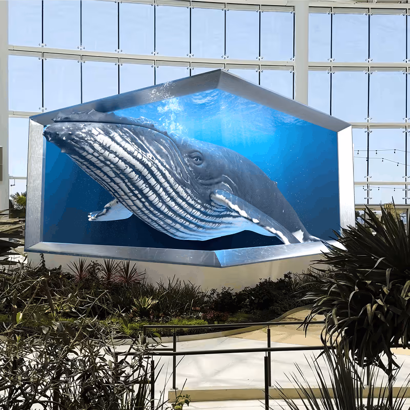 Large 3D digital display of a whale swimming underwater inside a modern indoor space with large windows and plants.