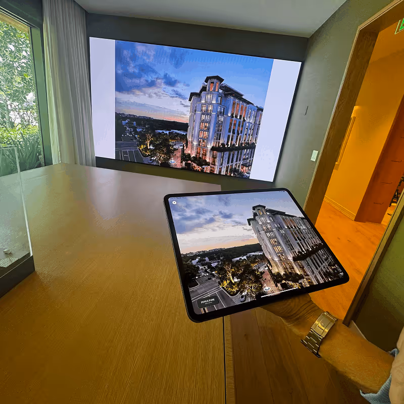 Person holding a tablet displaying a high-rise building image, matching the same building image projected on a wall screen.