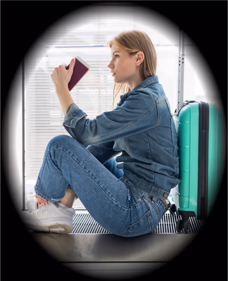 A woman sitting on a luggage bag with a book in her hand.