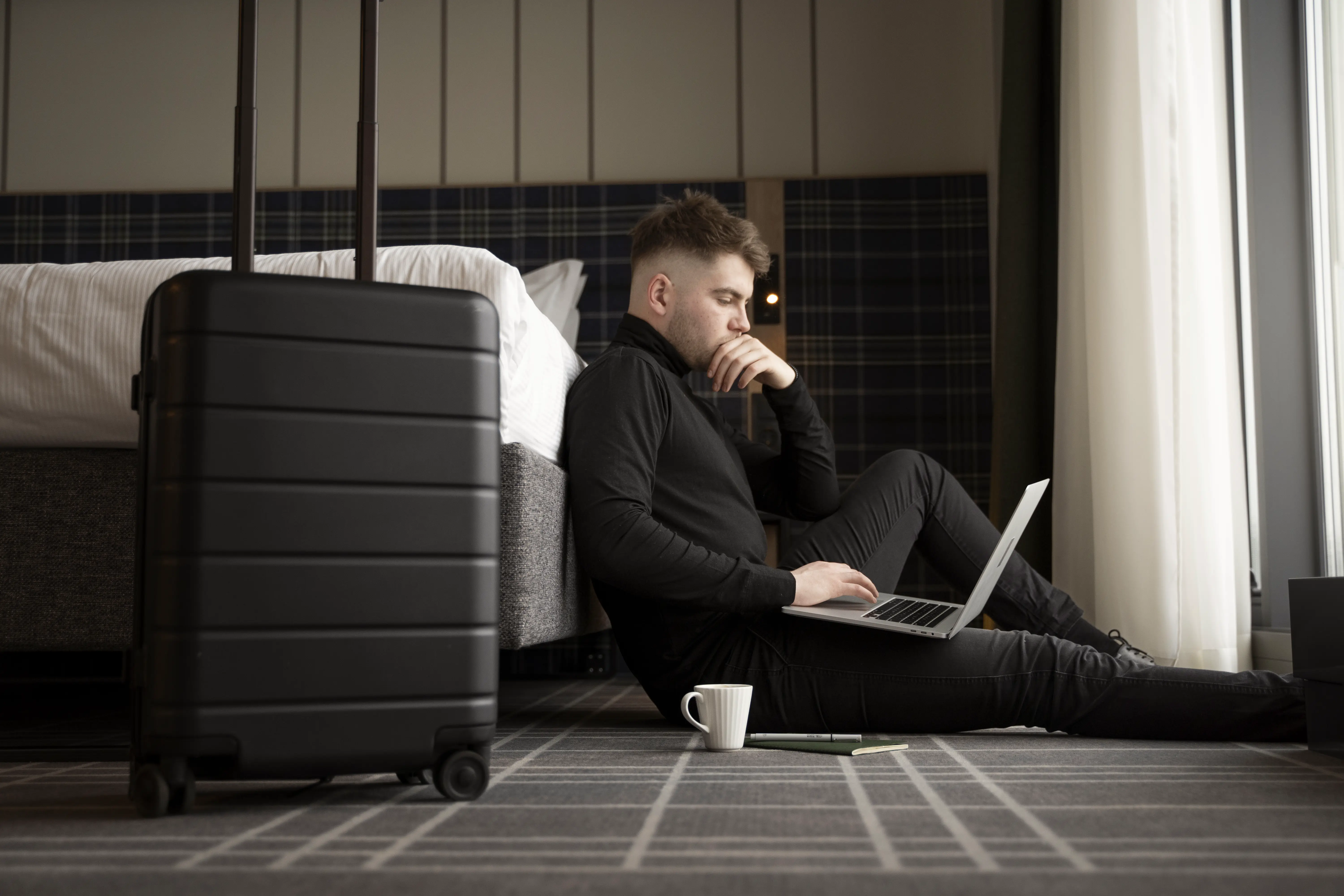 A man sitting on the floor with a laptop and a suitcase.