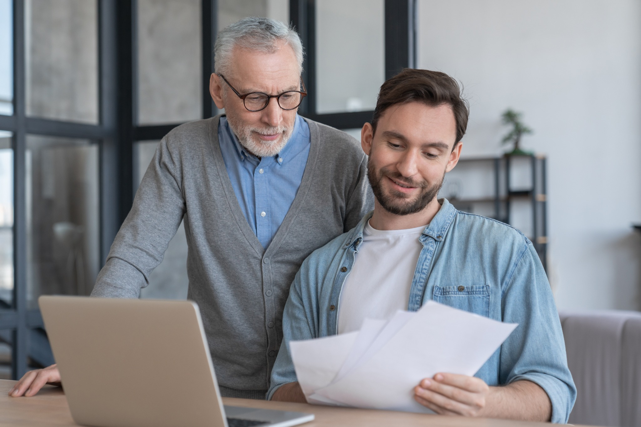 Older man and younger man reviewing documents together at a laptop