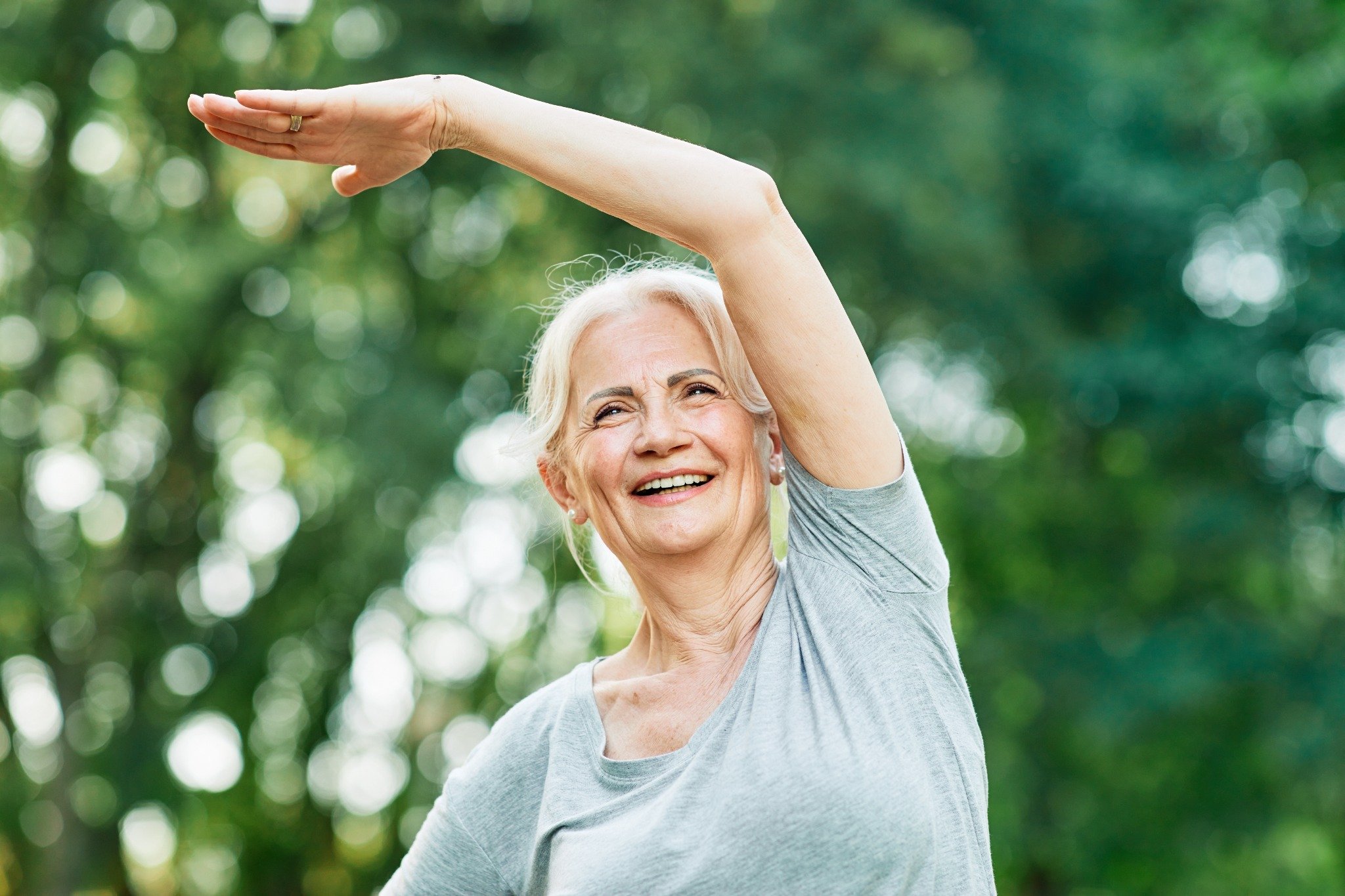 a smiling older woman outdoors in a green, natural setting