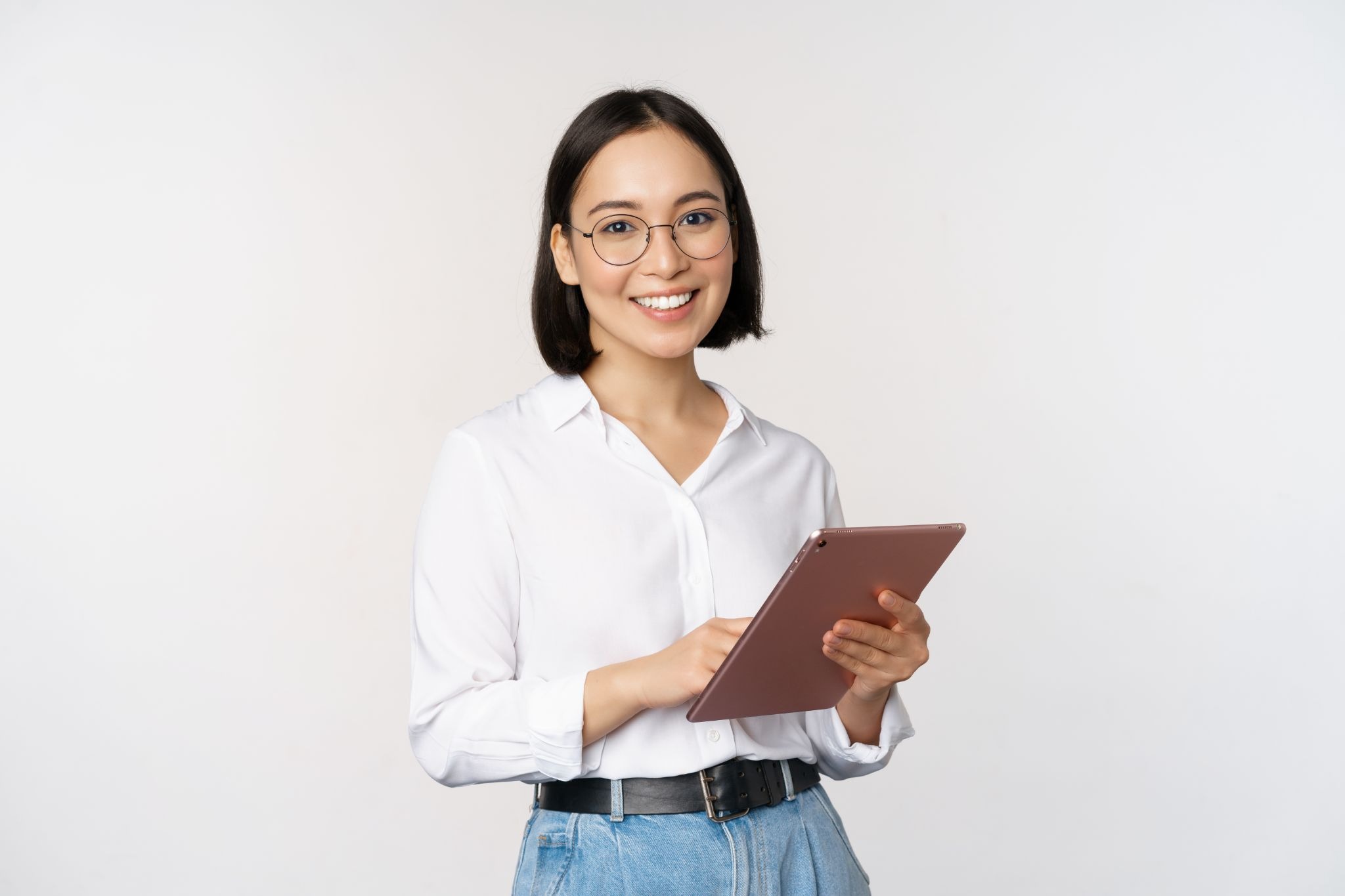 a young professional woman standing against a clean, light-colored background while holding a tablet.