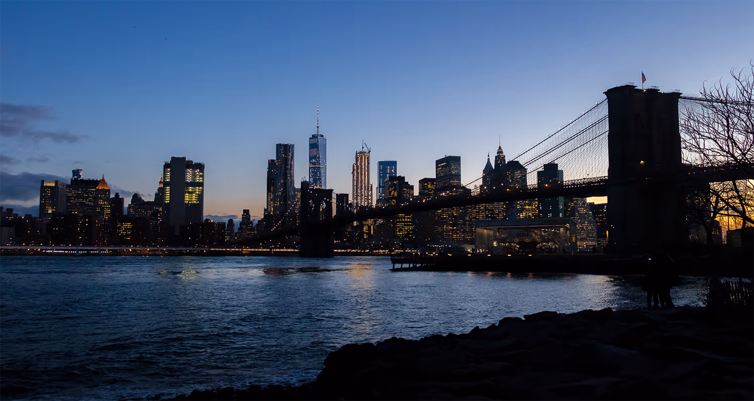 Panorama nočního velkoměsta s osvětleným Brooklynským mostem jako symbol elegance, velikosti a mezinárodní stability služeb makléře Eurovalley.
