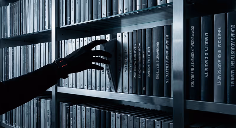 Ruka sahající pro složku v odborném archivu s tituly o pojištění a risk managementu, symbolizující snadný přístup k informacím přes klientský portál Eurovalley.