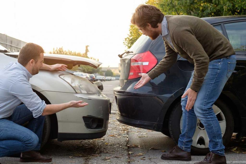 Two men inspecting damage after a car accident between a white and a black vehicle in a parking lot.