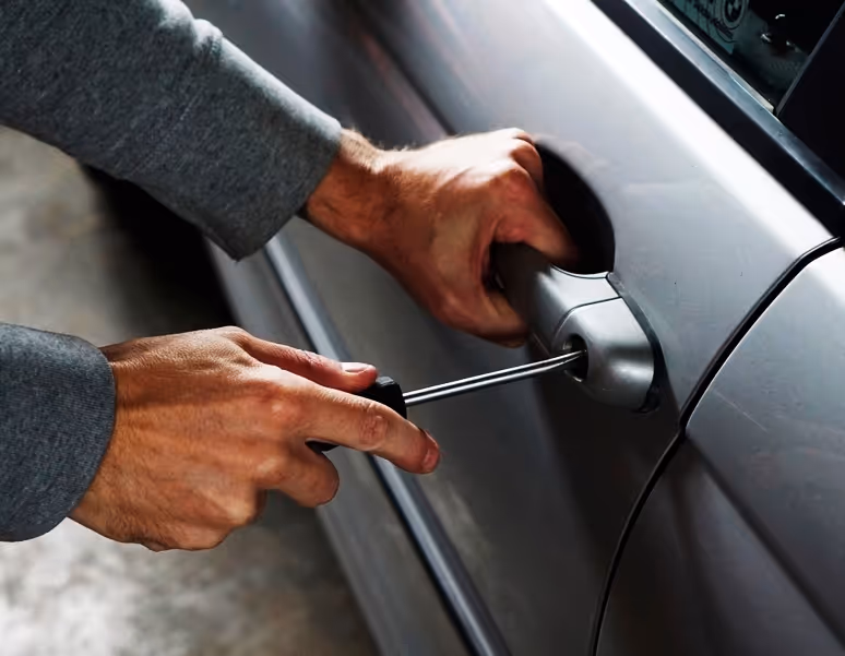 Close-up of hands using a screwdriver to forcibly open a car door lock.