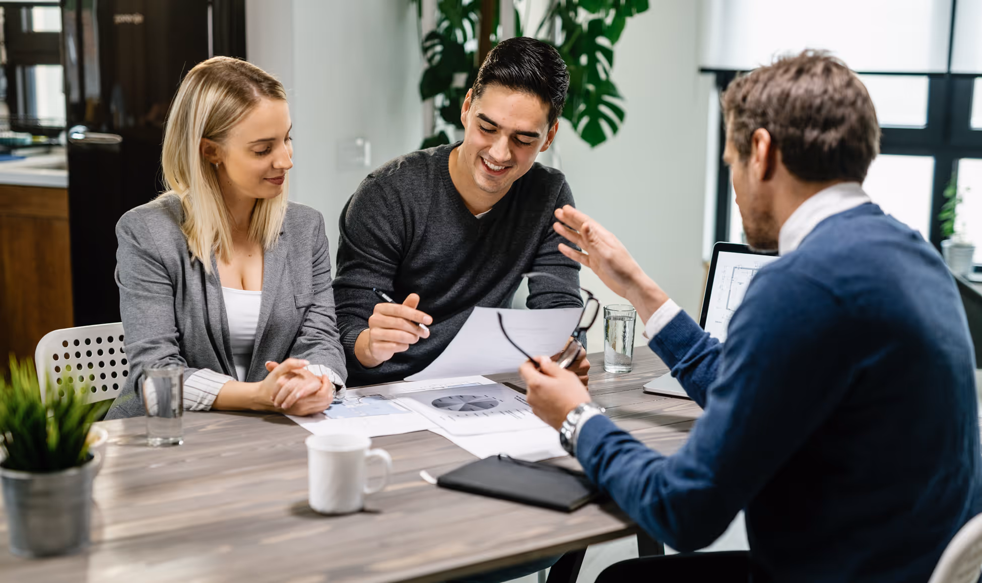 Two people reviewing documents with a professional explaining details at a table in an office.