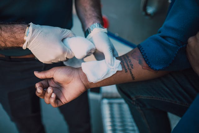 Person wearing gloves applies gauze to the forearm of another individual with a tattoo on their inner arm.