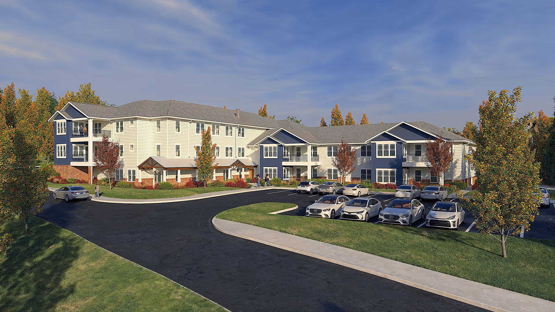 Modern two-story apartment building with white and navy siding surrounded by trees with autumn foliage and parked cars in front under a clear sky.