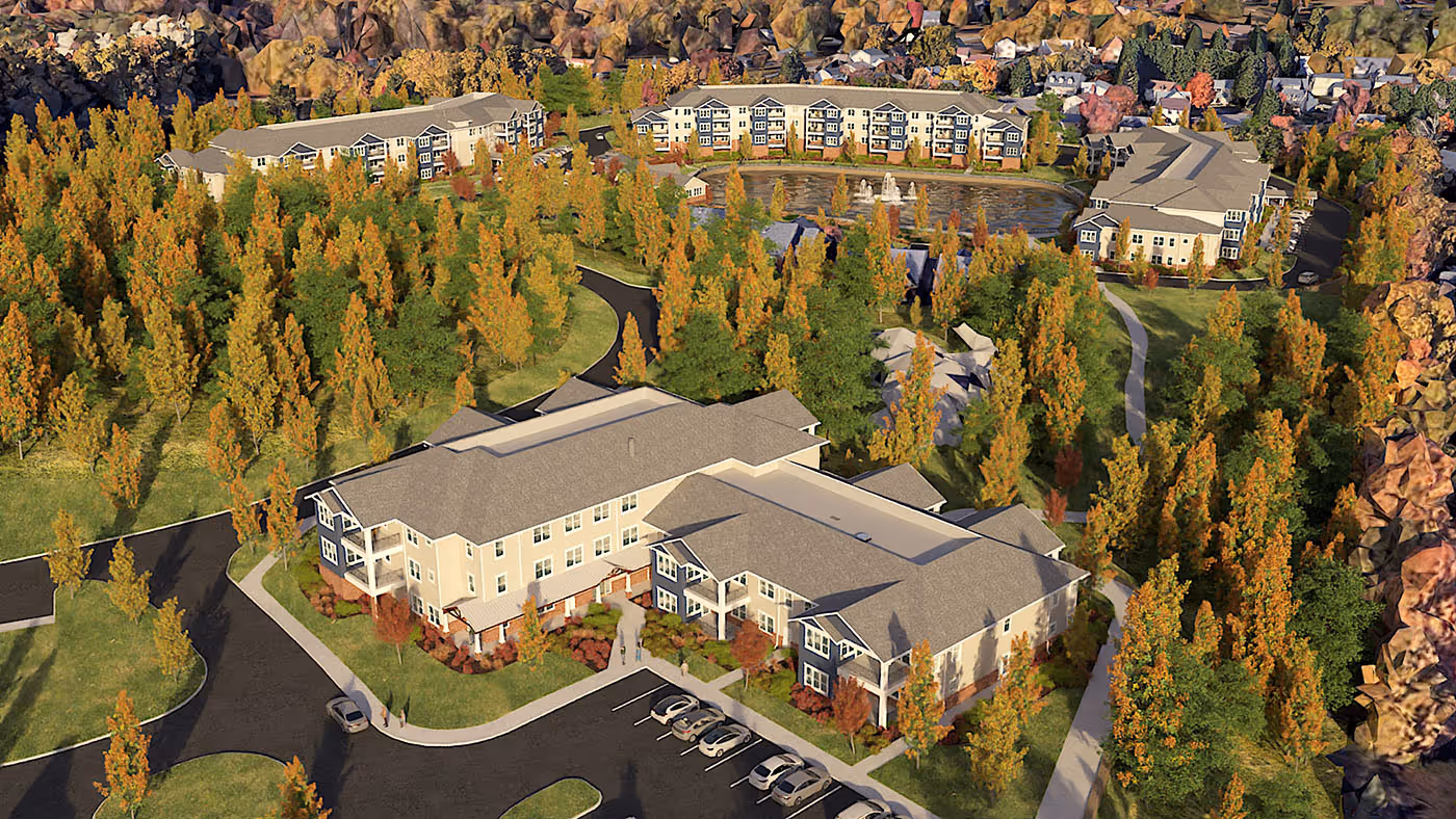 Aerial view of a residential complex surrounded by autumn trees with a pond and fountains in the background.