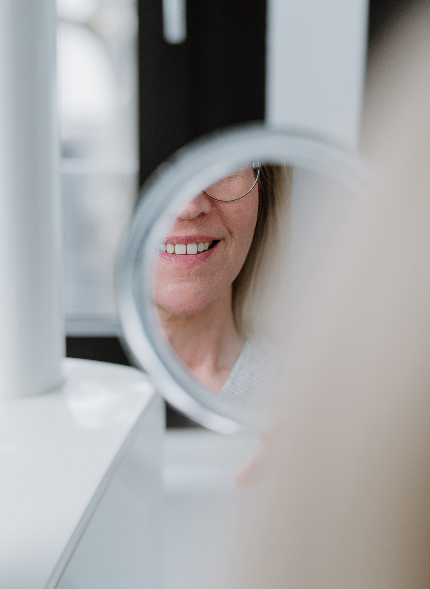 Spiegelbild eines lächelnden Gesichts einer Frau mit Brille.