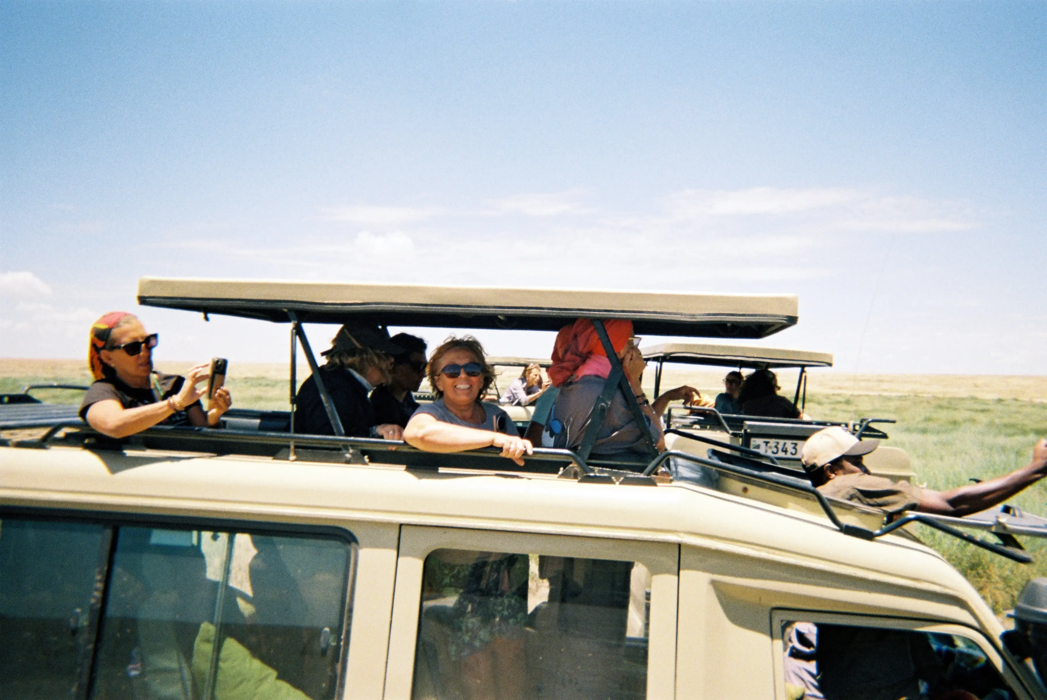 Tourists in safari vehicles with open roofs enjoying a sunny day in a grassy savanna.