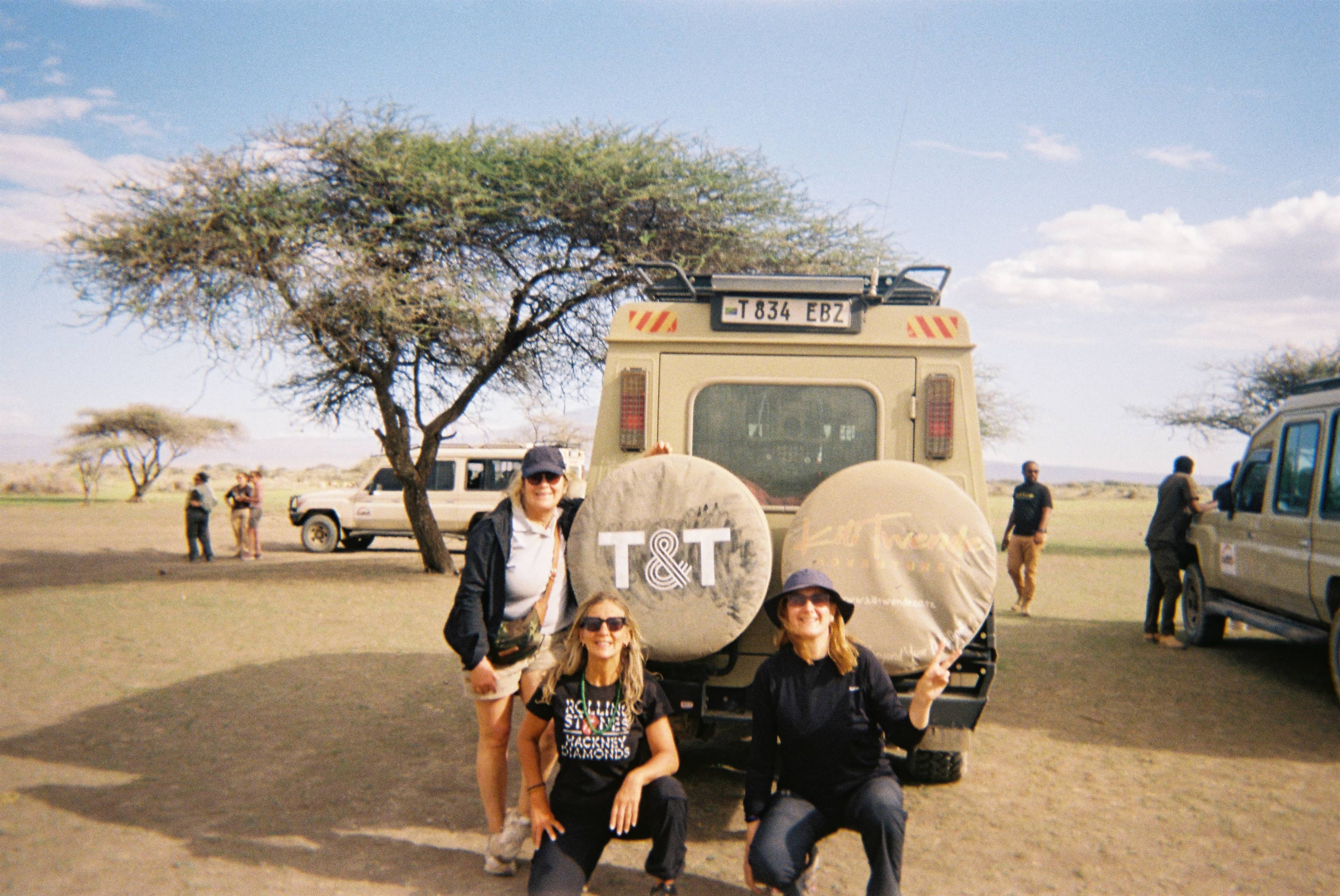 Safari vehicles with tourists observing wildlife on a grassy plain under a partly cloudy sky.