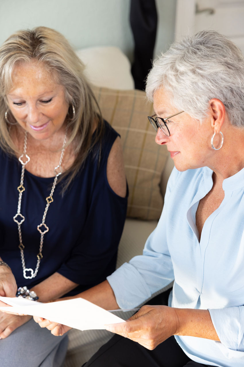 Two women seated together reviewing a document in a living room setting