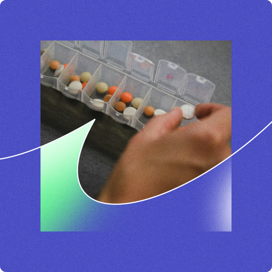 Hand organizing various colored pills in a clear plastic weekly pill organizer.