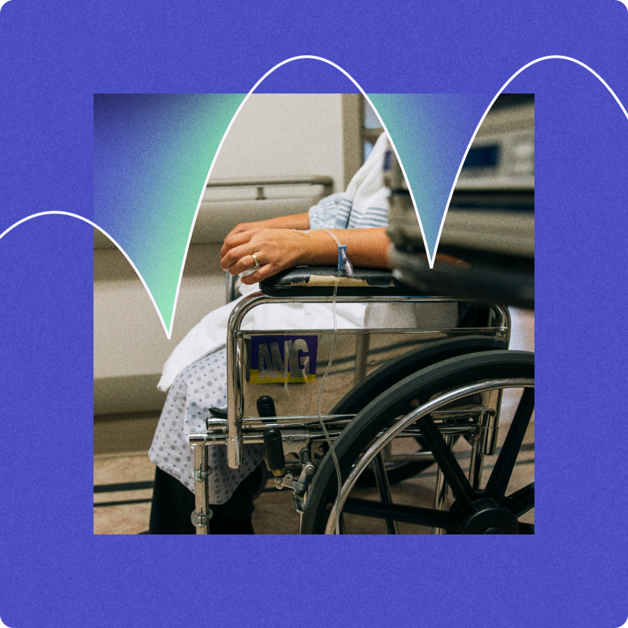 Person in hospital gown sitting in a wheelchair with an IV line attached to their hand.