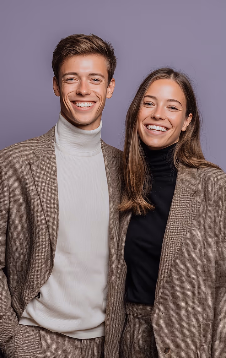 Smiling young man and woman standing side by side wearing brown checkered suits with turtlenecks.