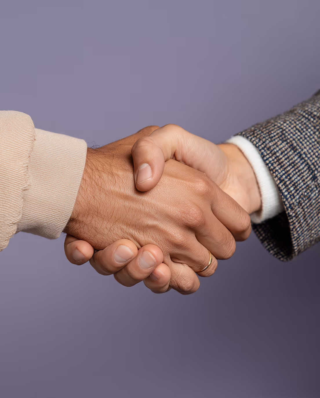Close-up of two people shaking hands against a purple background, one wearing a beige sleeve and the other a patterned jacket.