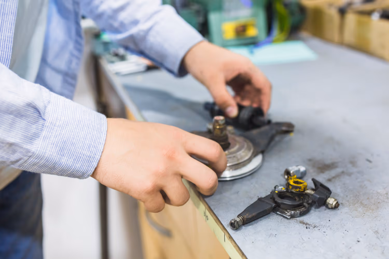 Person in striped shirt working on car parts on a workshop bench.