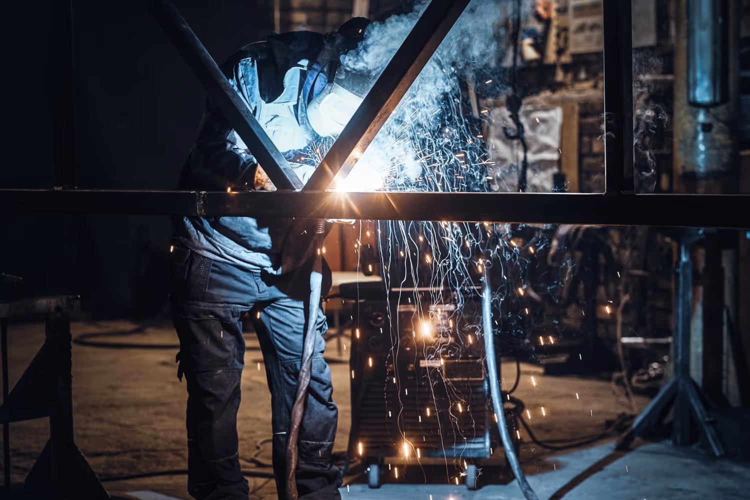 Worker welding metal beams indoors with bright sparks and smoke.