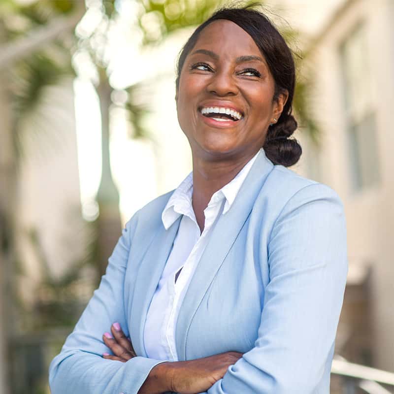 Smiling businesswoman in a light blue blazer with arms crossed outdoors.