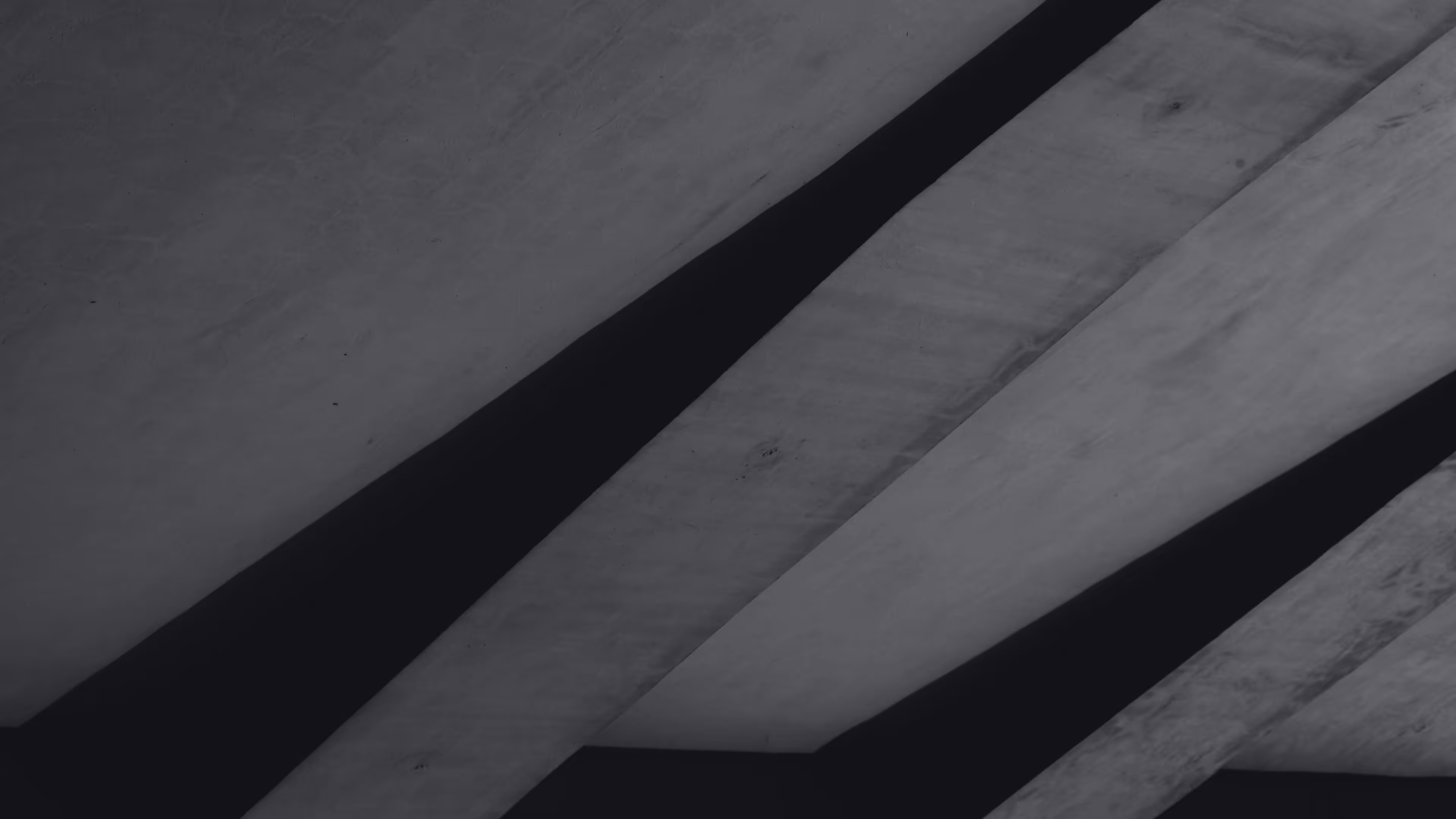 Close-up view of concrete beams with shadows creating diagonal lines in grayscale.
