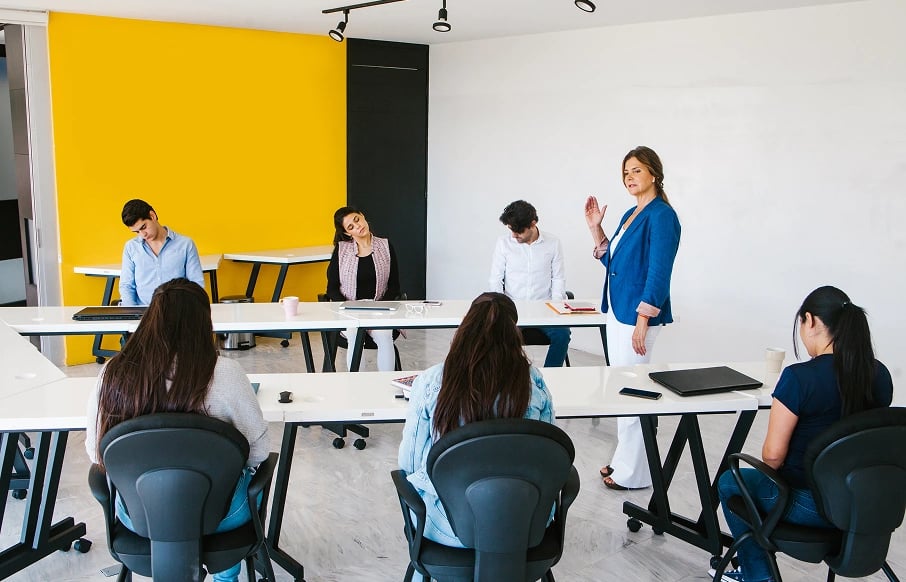 woman standing in middle of desks teaching to class