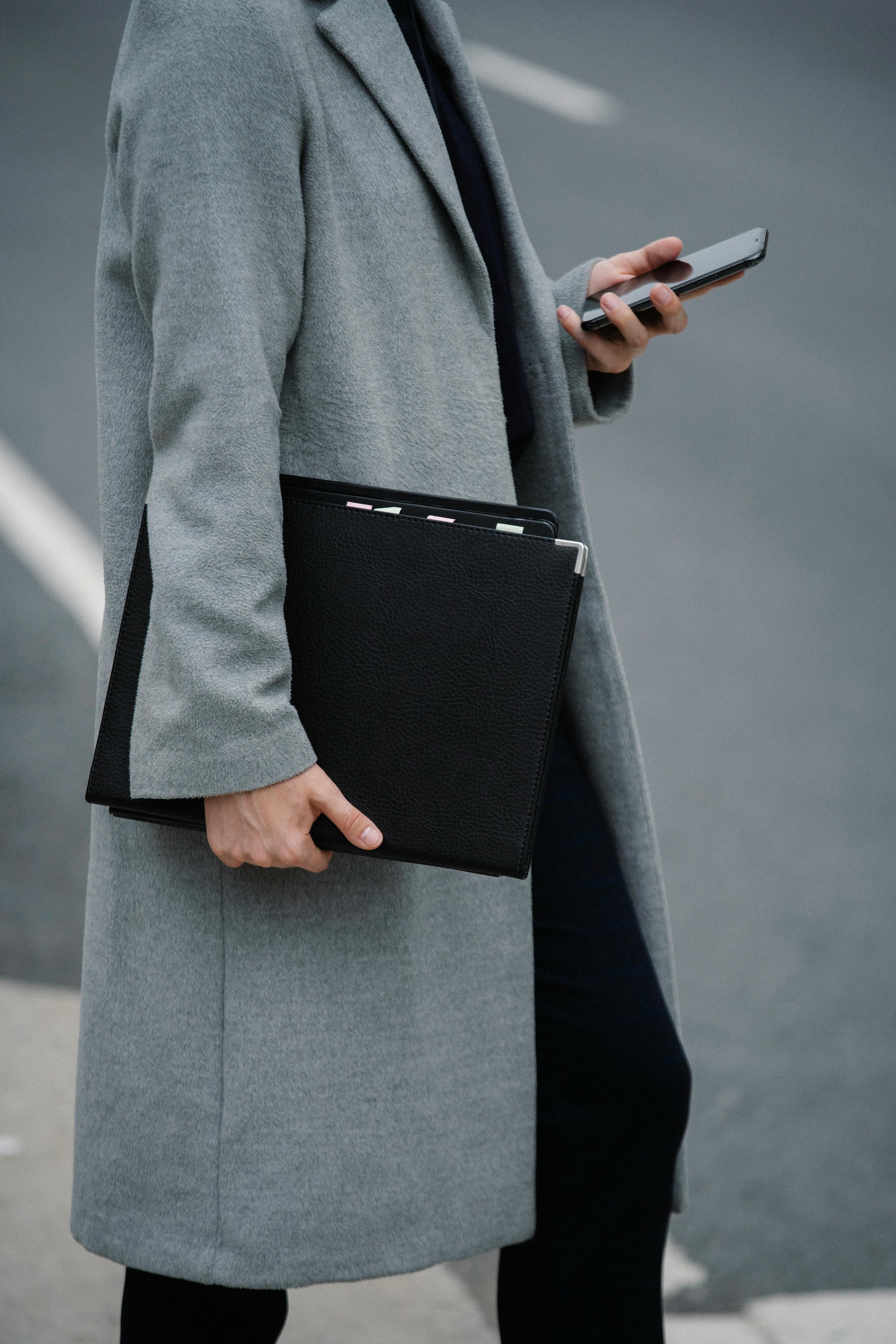 a professional man on his phone carrying documents for work wearing a long jacket