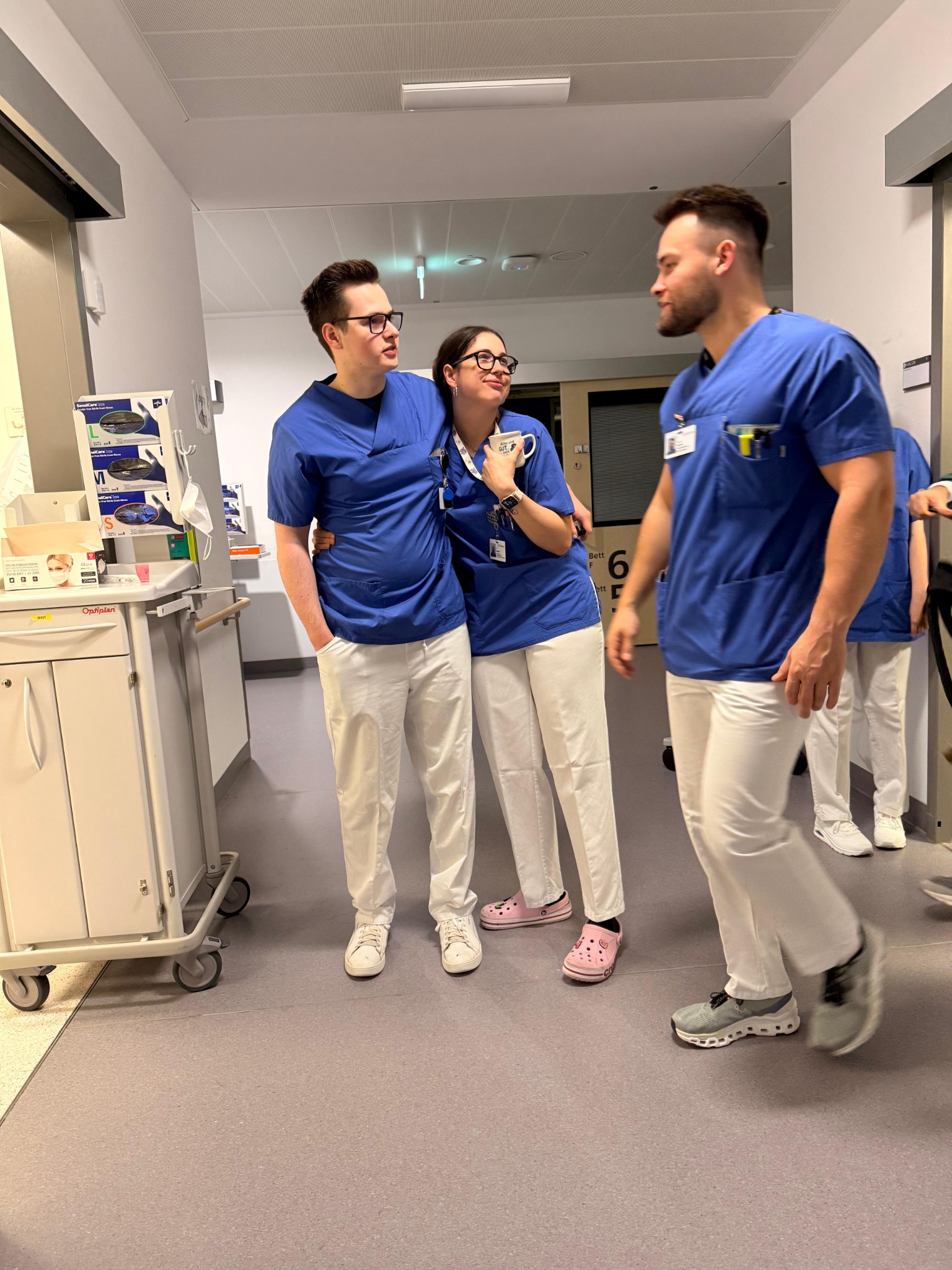 Drei Kolleginnen und Kollegen in blauer Pflegekleidung auf dem Klinikflur