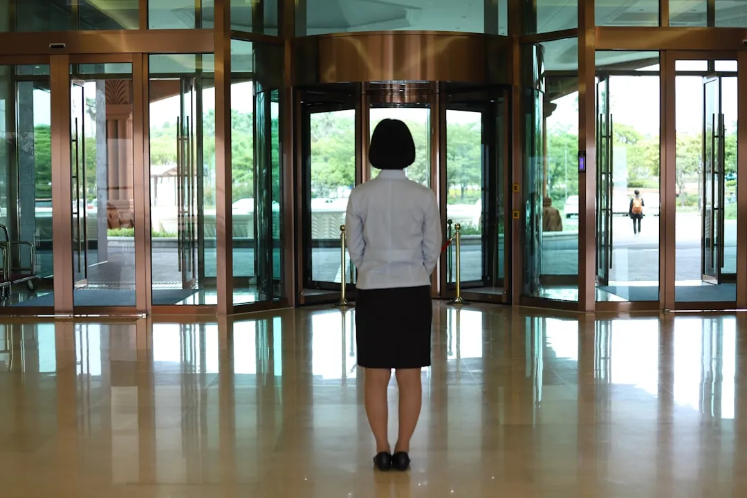 Corporate receptionist standing in a grand building entrance lobby near glass revolving doors